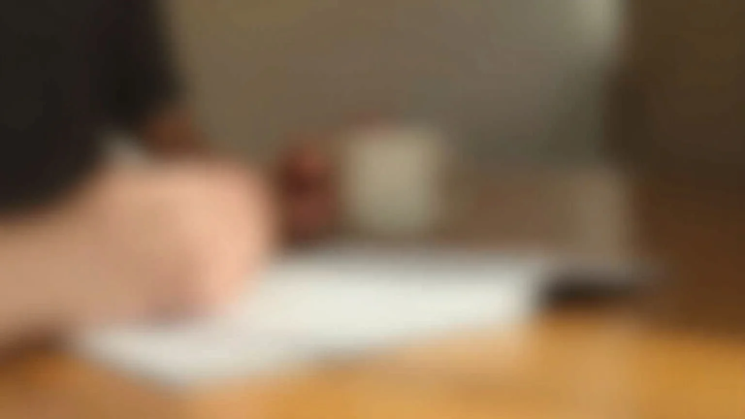 Solo professional reviewing client documents on a laptop with a notebook and coffee at a home office in warm afternoon light