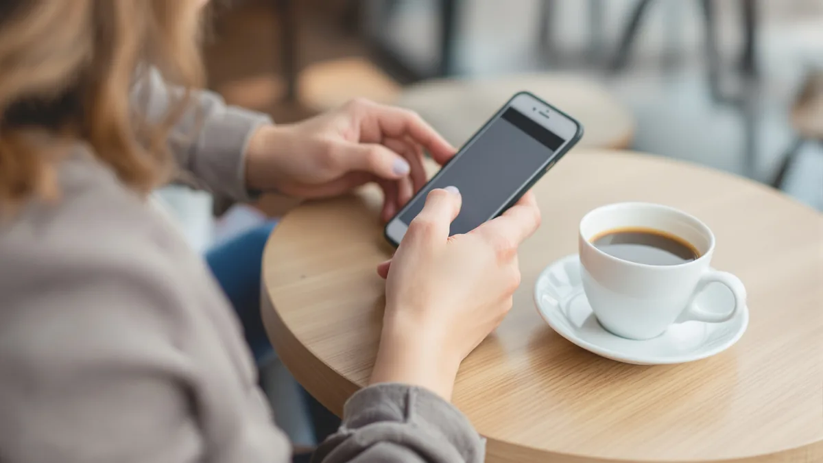 hands using ChatGPT on a phone next to a coffee cup